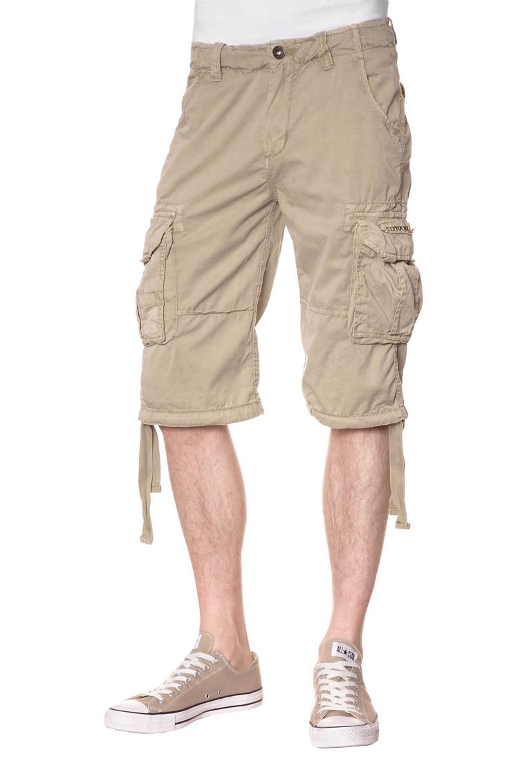 Pantaloni cargo beige con molte tasche, orli arricciati e un tessuto testurizzato. Indossati con sneakers beige, che mostrano gambe scoperte sotto il ginocchio.