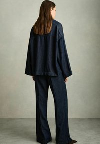 Dunkelblaue Jeansjacke mit lockerer Passform und abgesenkten Schultern, kombiniert mit weit geschnittenen, dunklen Jeanshosen, beide aus strukturiertem Stoff.