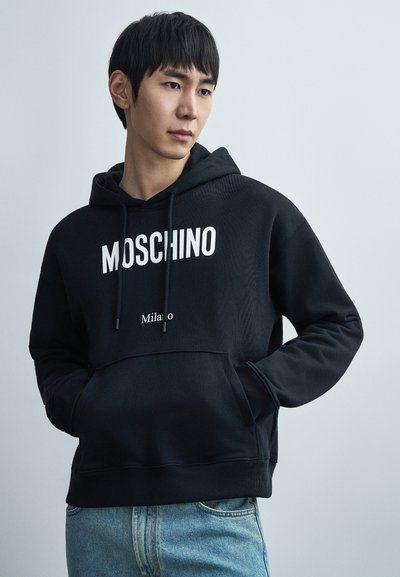 Sweat à capuche noir en mélange de coton, avec un grand logo blanc "MOSCHINO" et un texte plus petit "Milano". Comprend des cordons de serrage et une poche avant.