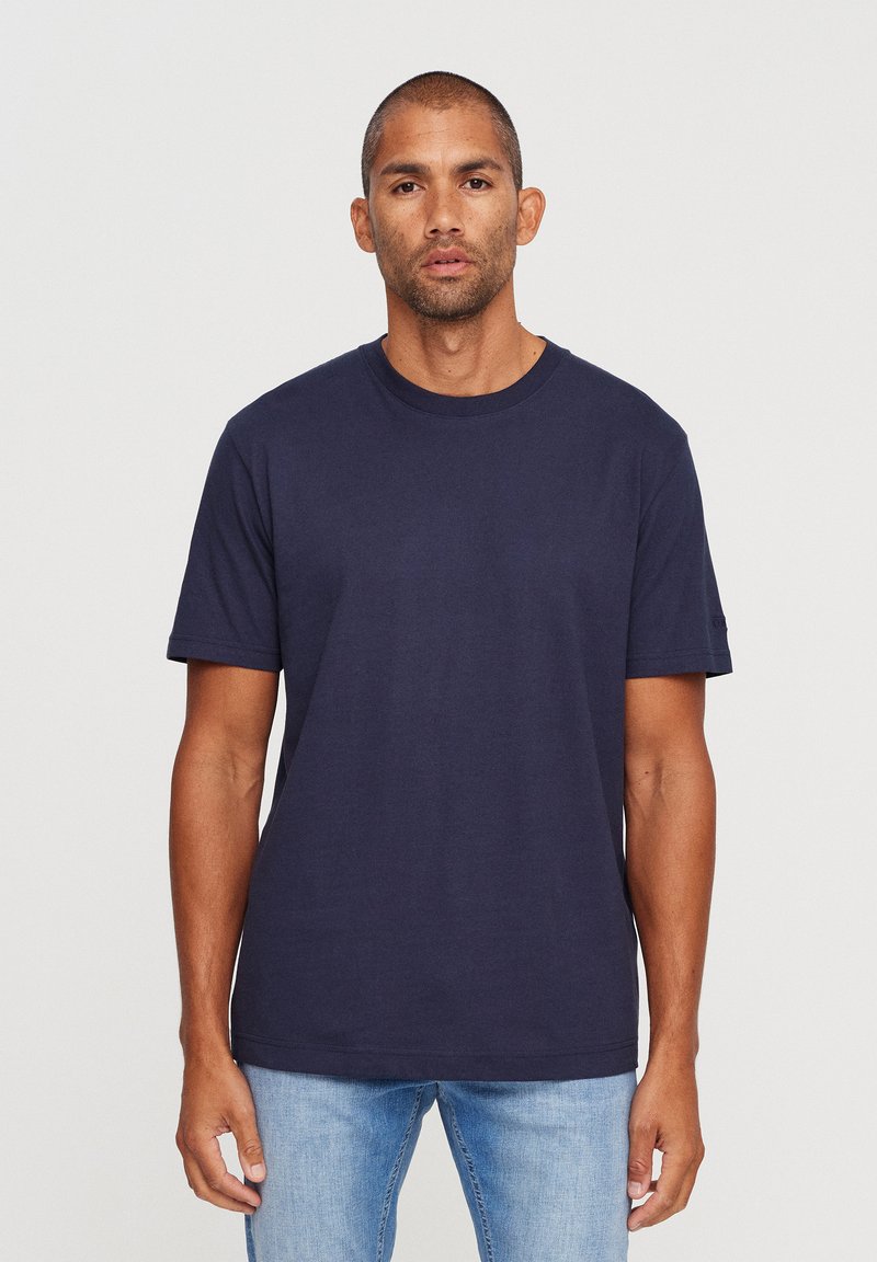 Navy blue cotton t-shirt with a round neckline and short sleeves, worn with light blue jeans; smooth texture, casual fit.