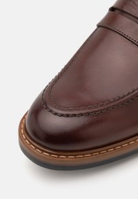 Braunes Leder Schuh mit einer glatten Oberfläche, runder Zehenpartie, sichtbaren Nähten und einer kontrastierenden hellbraunen Sohle mit dünnem Rand.