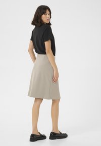Zwarte top met korte mouwen, beige rok tot de knie van een gladde stof, met een uitlopende vorm en zijzakken, gecombineerd met zwarte glanzende schoenen.