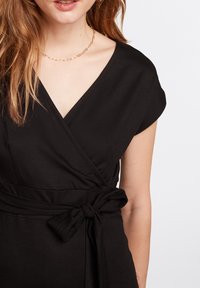 Robe noire portefeuille avec un décolleté en V et des manches courtes, dotée d'un détail de taille nouée. Fabriquée en tissu doux avec une texture lisse.