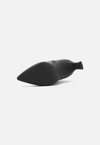 Svart spiss tå sko med en jevn finish, utstyrt med flat hæl og teksturert såle for grep, som viser minimalistisk design og rene linjer.