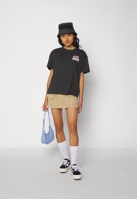 Black graphic t-shirt with a floral design, paired with a beige mini skirt, white socks, black and white sneakers, and a light blue handbag.