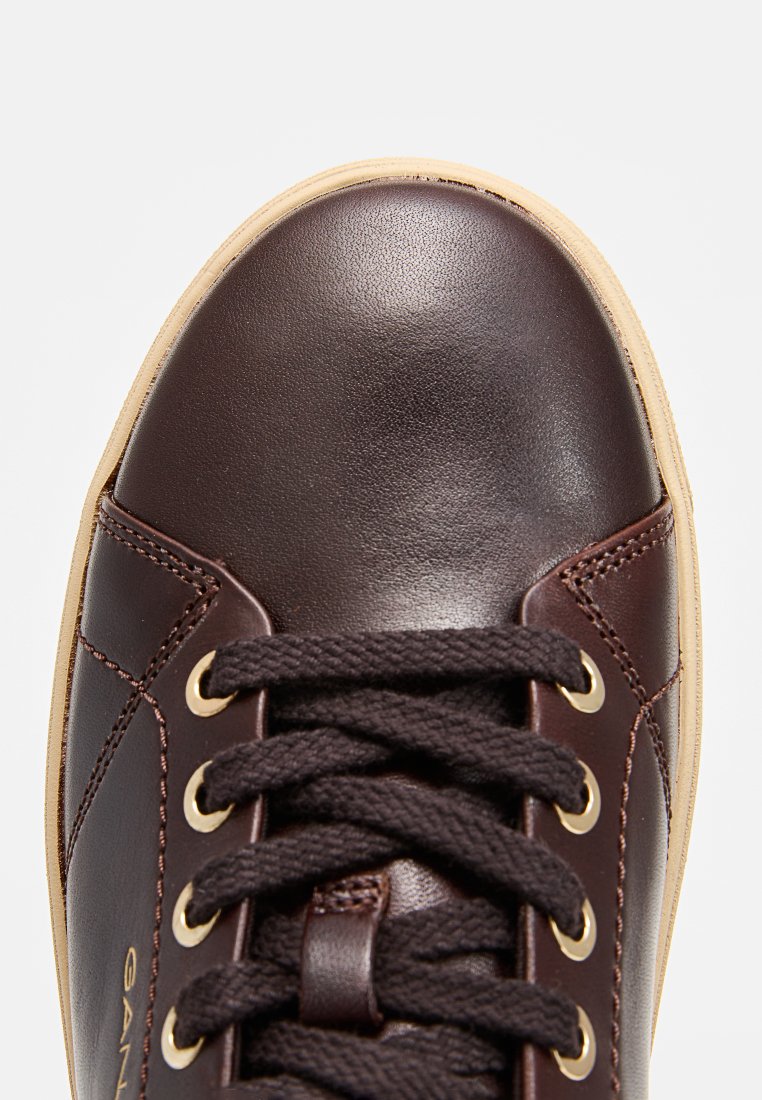 Dunkelbraune Leder-Sneaker mit runder Spitze, goldenen Ösen und dunklen Schnürsenkeln. Glatte Textur mit hellbraunem Gummisohle.