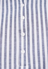 Tissu à rayures verticales blanches et bleues avec une rangée verticale de quatre boutons blancs cousus au centre.