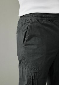 Pantaloni cargo gri închis cu talie elastică, având buzunare laterale și un buzunar cu fermoar pe picior, confecționați dintr-un material ușor.