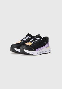 Een paar zwarte Skechers sneakers met witte zolen, paarse accenten, witte veters en merklabels op een effen lichte achtergrond.