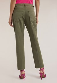 Oliwkowe spodnie o prostym kroju, z dwiema tylnymi kieszeniami. W połączeniu z różowymi sandałami na obcasie z paskami, które prezentują prosty design.