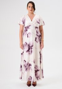 Langes, cremefarbenes Kleid mit lila Blumenmustern, volanten Ärmeln und taillierter Taille, aus leichtem Stoff gefertigt. Braune spitze Absätze.