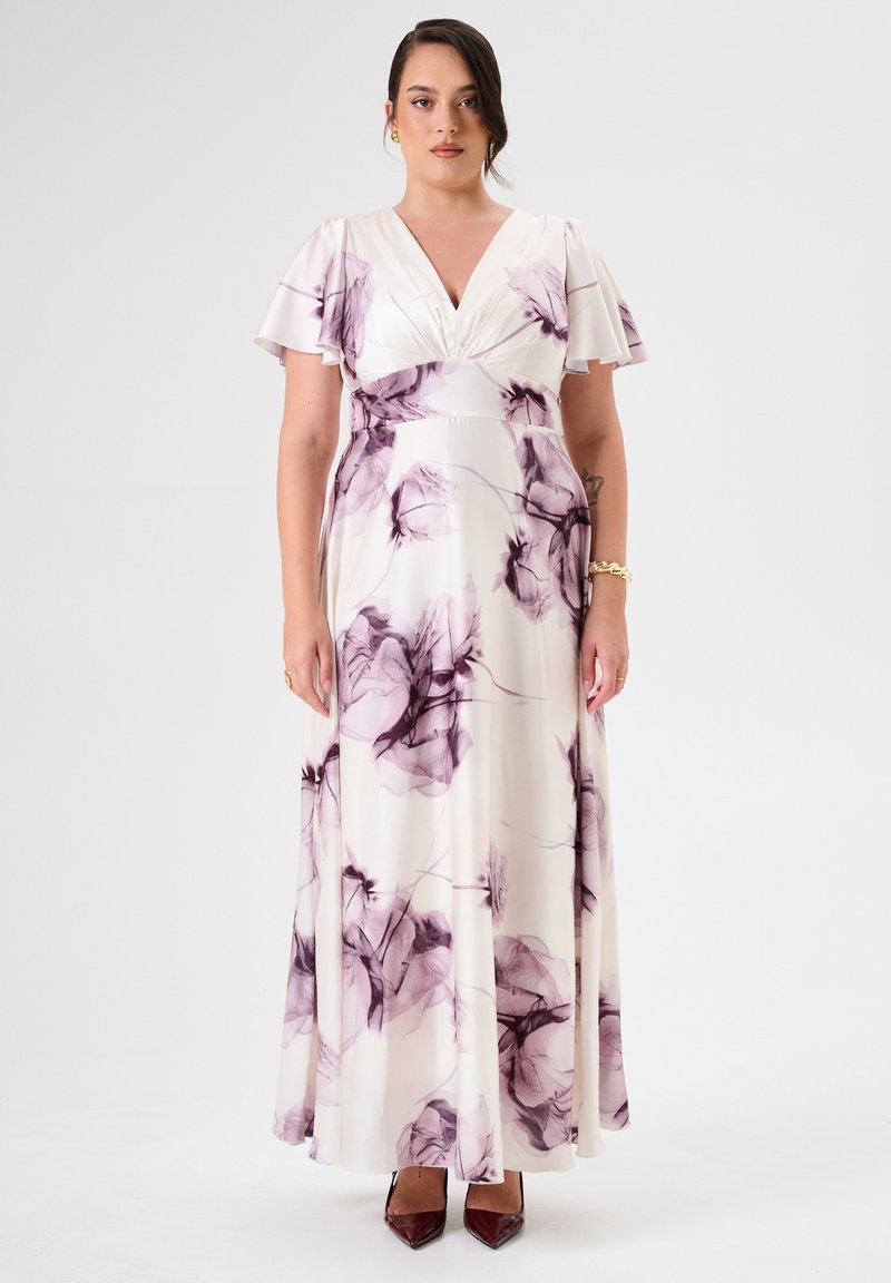 Langes, cremefarbenes Kleid mit lila Blumenmustern, volanten Ärmeln und taillierter Taille, aus leichtem Stoff gefertigt. Braune spitze Absätze.