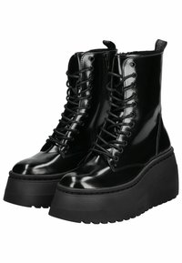 Botas de combate de charol negro con suela de plataforma gruesa, punta redondeada y cordones delanteros. Presentan una lengüeta y detalles de costura sutiles.