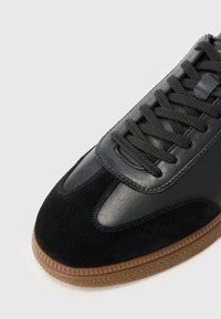 Baskets noires en cuir et daim avec une finition lisse, bout arrondi et semelle en caoutchouc texturé. Présente des lacets plats noirs et des coutures de détail.