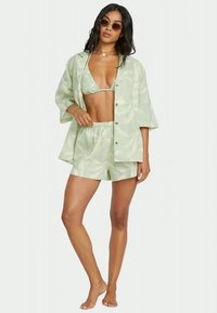 Vaaleanvihreä, kuviollinen pyjama-asusetti, johon kuuluu lyhythihainen paita, bikinitoppi ja shortsit pehmeästä, hengittävästä kankaasta; pyöreät aurinkolasit asusteena.