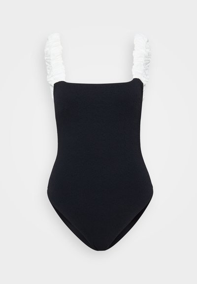 Black one-piece swimsuit with a textured fabric, featuring white ruffled straps. Rectangular neckline and a high cut leg design.