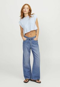 Top cropped sin mangas de color azul claro y jeans de mezclilla de pernera ancha con cintura con cordón. Los jeans presentan un lavado claro y un corte casual.