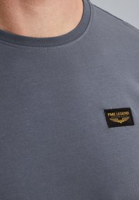 Siva bombažna majica s okroglim ovratnikom, ki ima črn tekstilni znak z zlatim vezenjem z napisem "PME Legend American Classic."