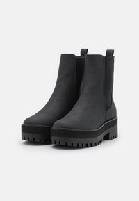 Black ankle boots with a smooth, faux suede finish, elastic side panels, and a chunky, ridged sole for added height and grip.