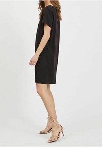 Svart kortärmad klänning med avslappnad passform, knälängd. Matchad med beige, strappy högklackade sandaler. Slät tygtextur.