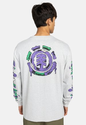 Man with short dark hair wears light gray long-sleeve shirt with large purple and green abstract graphic on back and both sleeves.