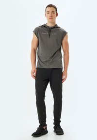 Grijze mouwloze hoodie met een bedrukte ontwerp, gecombineerd met zwarte tapered sportbroeken met paneelstiksels en zwarte sneakers.