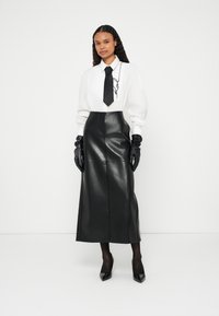 Camicia bianca con cravatta nera con un motivo distintivo, abbinata a una gonna midi in pelle nera e guanti lunghi neri. Scarpe con tacco alto.