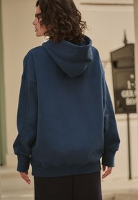 Übergroßer blauer Hoodie mit Kordelzugkapuze, elastischen Bündchen und Saum. Weicher Stoff mit glatter Textur. Keine sichtbaren Muster oder Akzente.