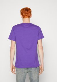 Lila bomull T-shirt med kort ärm och rund halsringning, med rak nederkant och minimal detaljering. Bärs med ljusblå jeans.