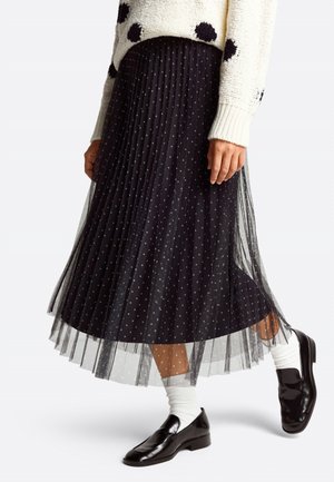Schwarzer, plissierter Midirock mit Polka-Dots, aus durchsichtigem Material. Gestylt mit einem Pullover, weißen Socken und schwarzen Loafers.