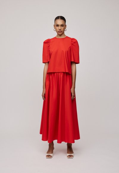 Rotes Zweiteiler-Outfit mit einem kurzärmeligen Oberteil mit Puffärmeln und einem langen, fließenden Rock. Der Stoff scheint glatt und leicht zu sein.