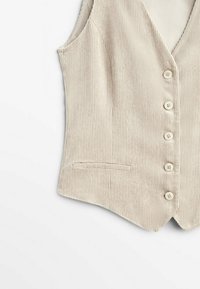 Gilet sans manches en velours côtelé beige avec cinq boutons devant et une petite poche passepoilée sur le côté gauche.