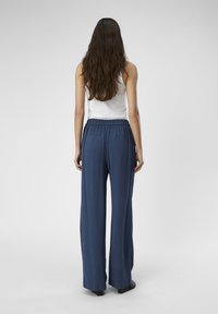 Pantalons larges bleu marine avec une coupe ample, fabriqués en tissu doux. Dotés d'une taille élastique et de deux poches arrière.