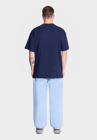 Granatowa bawełniana koszulka z krótkim rękawem, luźny krój i okrągły dekolt; noszona z jasnoniebieskimi luźnymi dżinsami i trampkami.