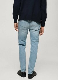 Lichtblauwe slim-fit jeans met achterzakken, gecombineerd met een marineblauwe trui. De outfit wordt compleet gemaakt met zwarte schoenen.