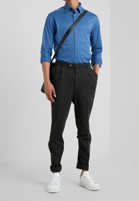 Camicia blu a maniche lunghe con bottoni, pantaloni plissettati antracite, sneakers bianche e borsa a tracolla nera. Tessuto liscio e vestibilità su misura.