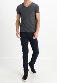 Camiseta de hombre de cuello en V en gris oscuro, hecha de algodón. Combinada con pantalones azul marino, con los puños enrollados, y zapatillas negras. Diseño simple.