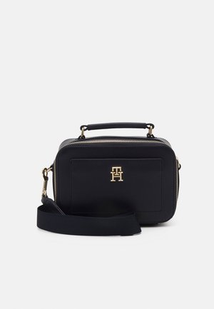 Sac bandoulière rectangulaire en cuir noir avec poignée supérieure, fermeture éclair dorée, logo doré sur le devant et large bandoulière amovible.