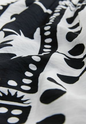 Schwarz-weißer Stoff mit einem abstrakten Muster aus Formen, Linien und Punkten. Das Material scheint leicht und strukturiert zu sein.