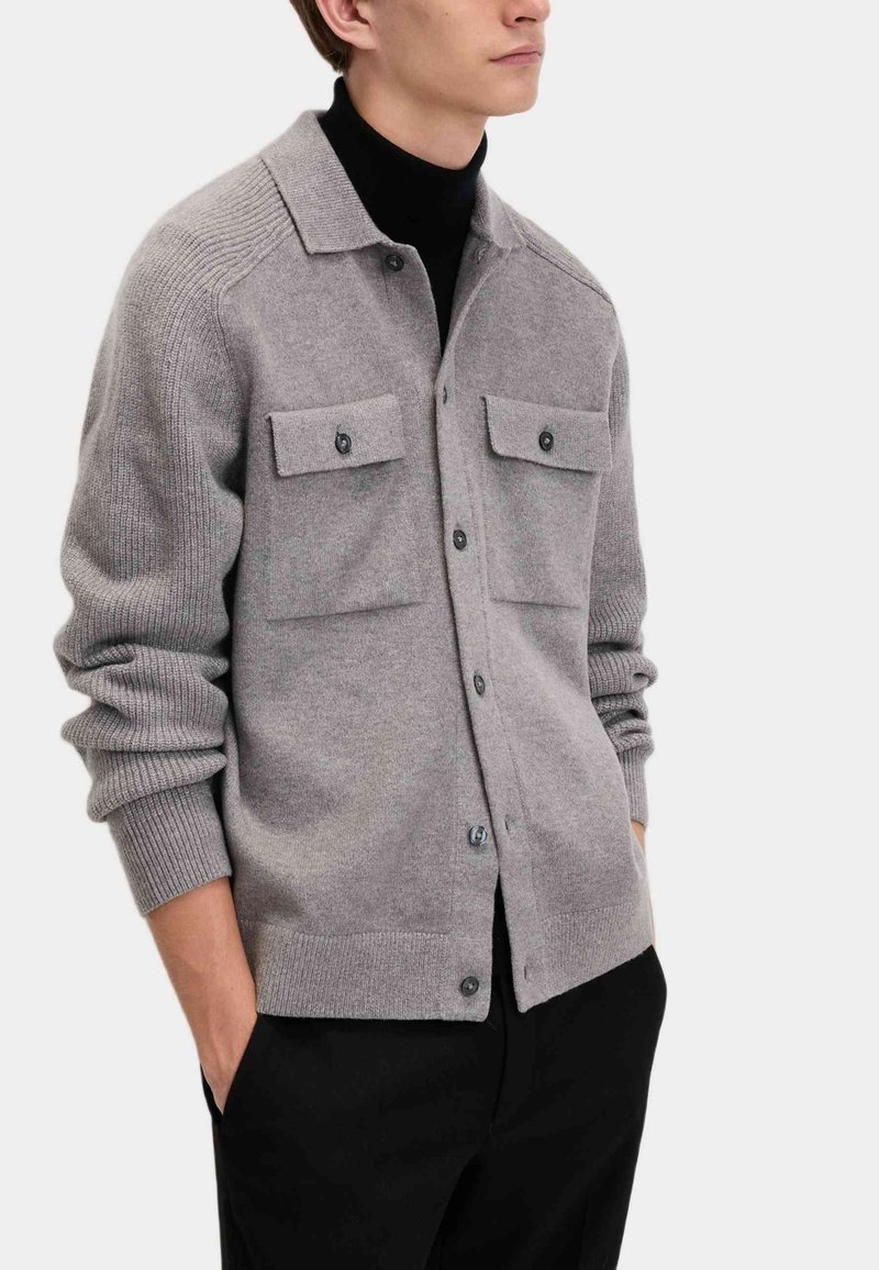 Szary dzianinowy kardigan z dwoma przednimi kieszeniami, zapięciem na guziki i ściągaczami przy mankietach. Miękka faktura i luźny krój zwiększają komfort noszenia.