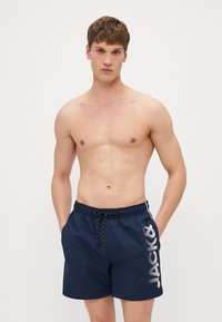 Marineblaue Badehose aus leichtem Material, mit einem Kordelzug am Bund und einem großen weißen Logo auf der linken Seite.