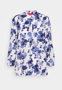 Blusa a maniche lunghe bianca con motivo floreale blu, dotata di collo alla mandarino e chiusura frontale con bottoni. Tessuto morbido e leggero.