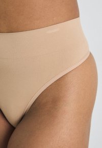 Beige high-waisted brief with a smooth, stretchy texture and no visible seams, featuring a wide, soft waistband for comfort and fit.