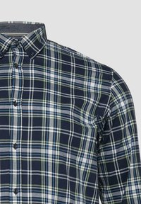 Navyblaues, weißes, graues und grünes kariertes Hemd mit Knöpfen und einem Button-Down-Kragen, dargestellt vom Brustbereich bis zur rechten Schulter.