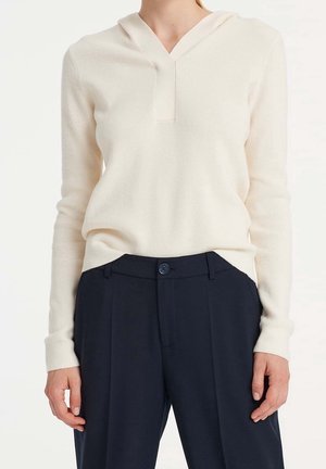Cremefarbener, gerippter Pullover mit V-Ausschnitt und Kapuze. Besitzt lange Ärmel und wird mit navy Farbenen Hosen mit Knopfverschluss kombiniert.