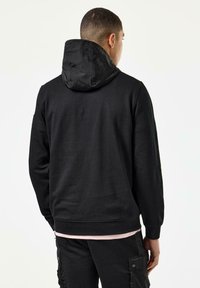 Sort hættetrøje med en kontrasterende sort nylonhætte, ribbede manchetter og kant, båret over en lys pink skjorte, har en afslappet pasform.