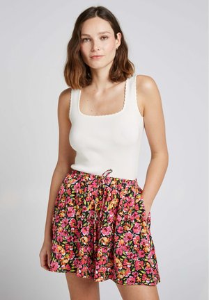 Débardeur côtelé blanc avec un décolleté carré, associé à une jupe noire ornée d'un motif floral coloré et d'une taille à cordon.