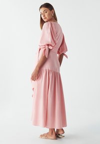 Puff-sleeve, pink maxi dress with a tied waist and tiered skirt. Features a smooth fabric with a soft texture and flowing design.