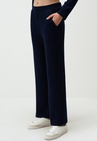Navy ribbed knit pants featuring a relaxed fit, wide legs, two side pockets, and a comfortable elastic waistband, paired with white sneakers.