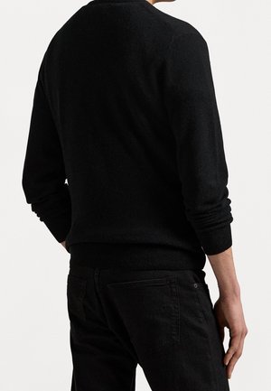 Mężczyzna ubrany w dopasowany czarny sweter z długim rękawem i czarne spodnie, pokazany od tyłu na neutralnym tle.